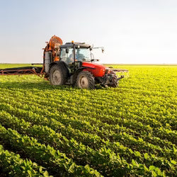 Red tractor spraying a field of crops under a clear sky