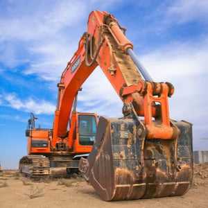 Large orange excavator on a construction site with a blue sky.